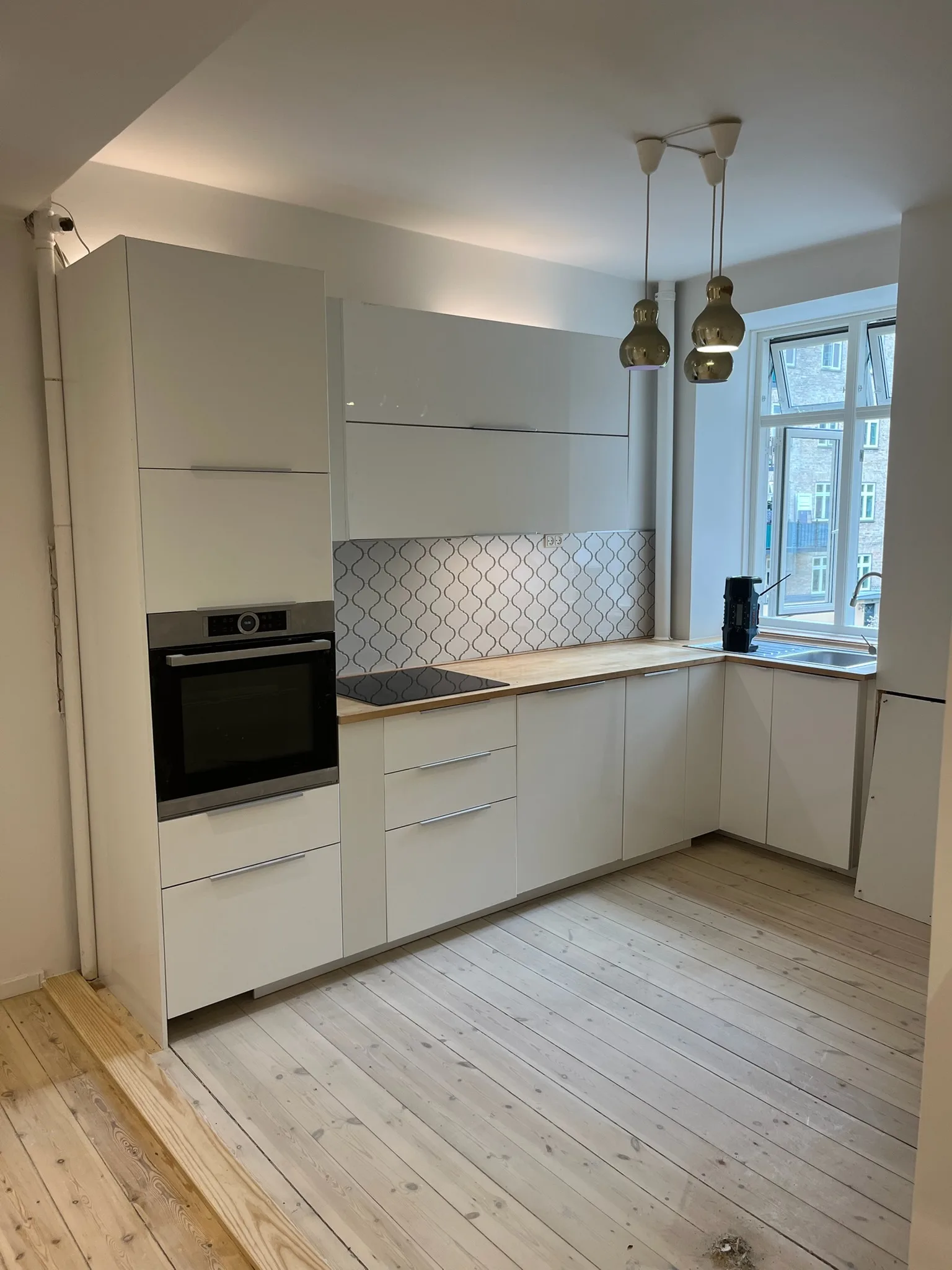 Færdigt hvidt køkken med flisevæg og messingpendler efter renovering