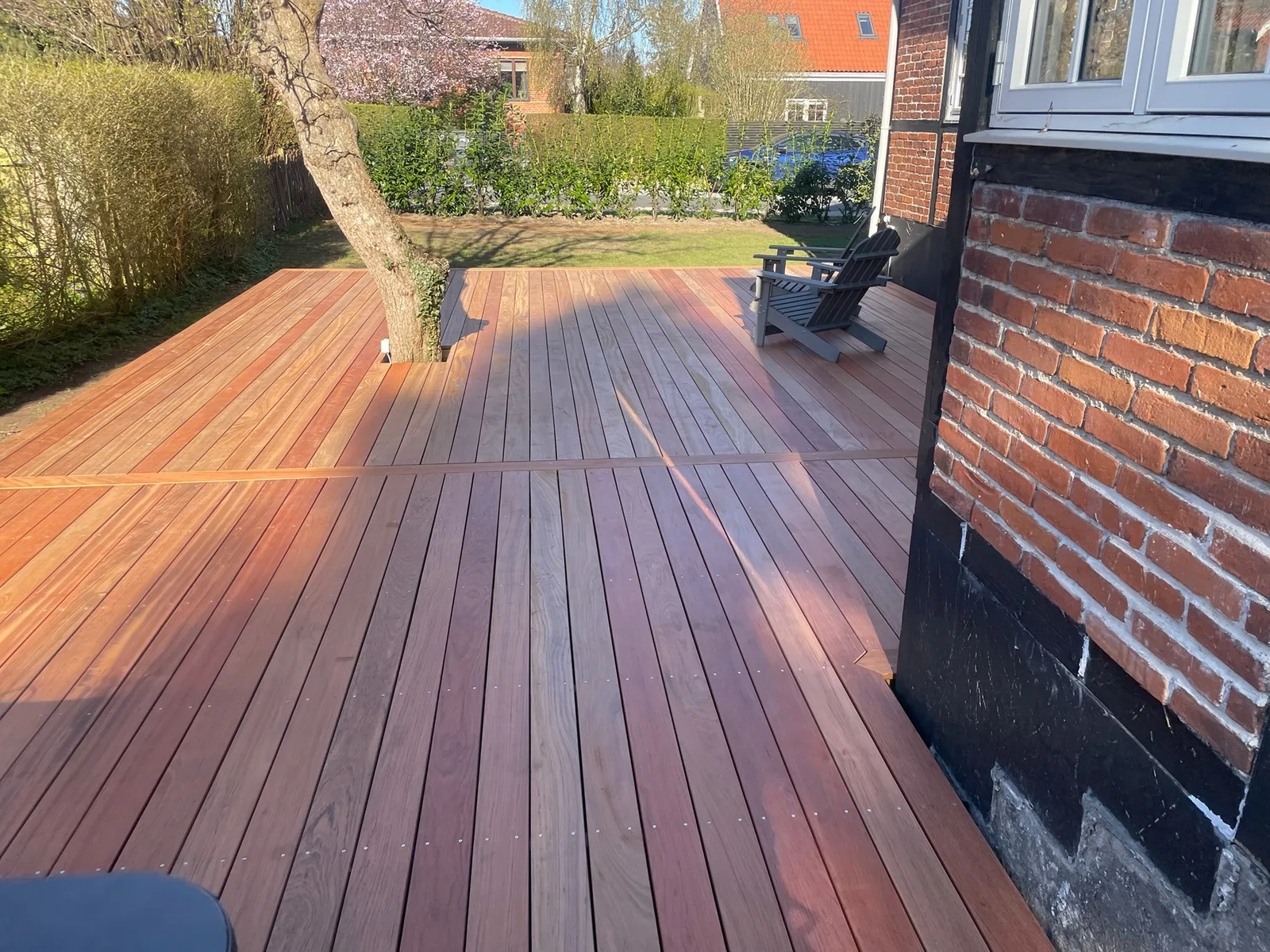 Hårdttræ-terrasse i aftenlys ved blomstrende træ og bindingsværkshus
