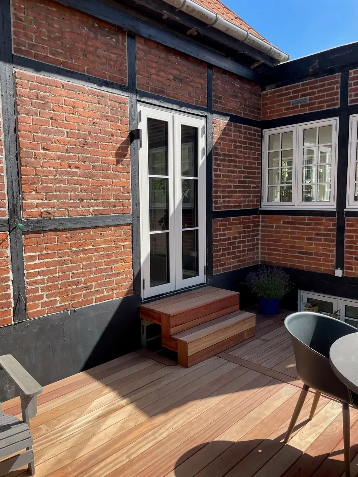 Ny hårdttræ-terrasse med trin i solrig gårdhave med bindingsværk