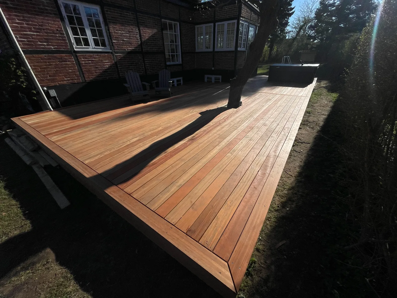 Vinklet hårdttræ-terrasse med loungestole ved muret hus