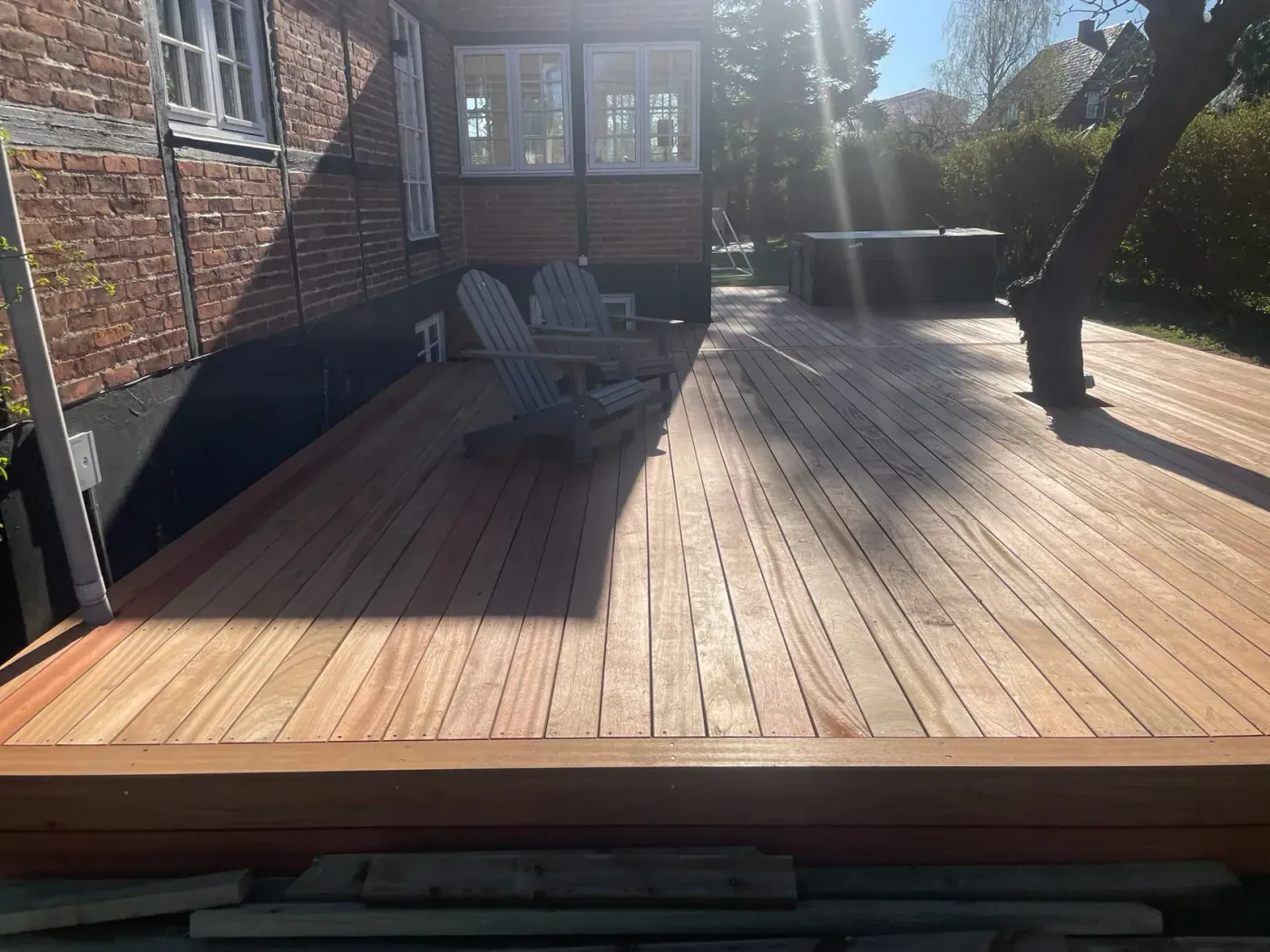 Hårdttræ-terrasse med loungestole og spabad i solrig have